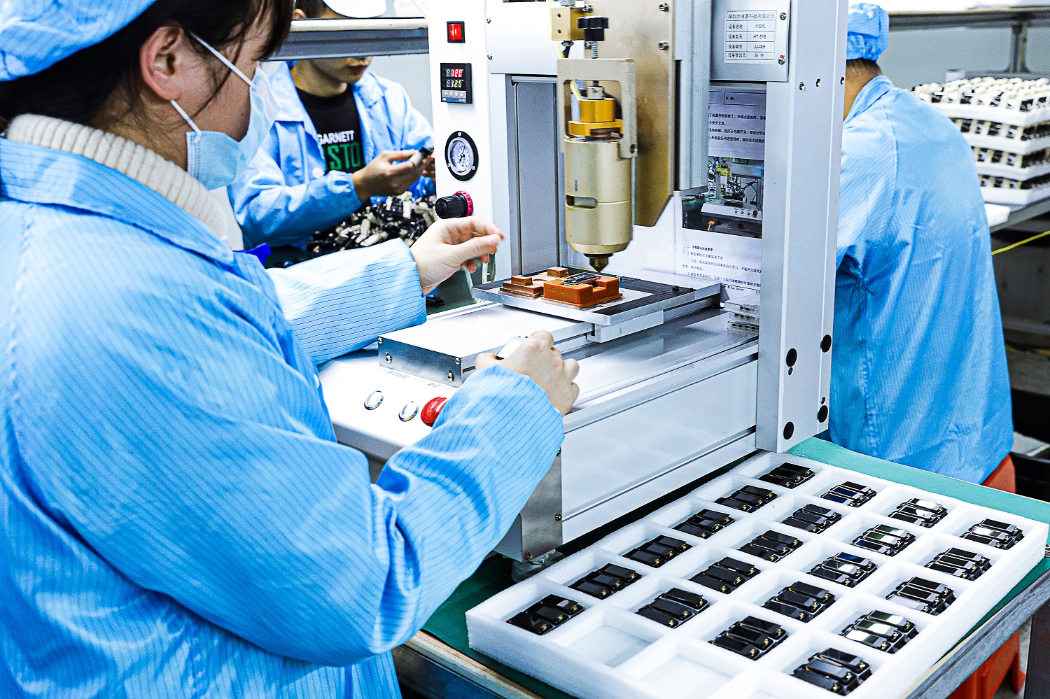Operators assembling smart watches at benches with tester jigs