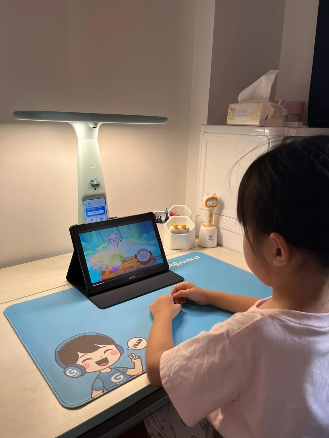 Child using a learning tablet at a desk, viewed from behind